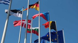 Mehrere Flaggen der EU-Mitgliedstaaten hängen an einem Fahnenmast.