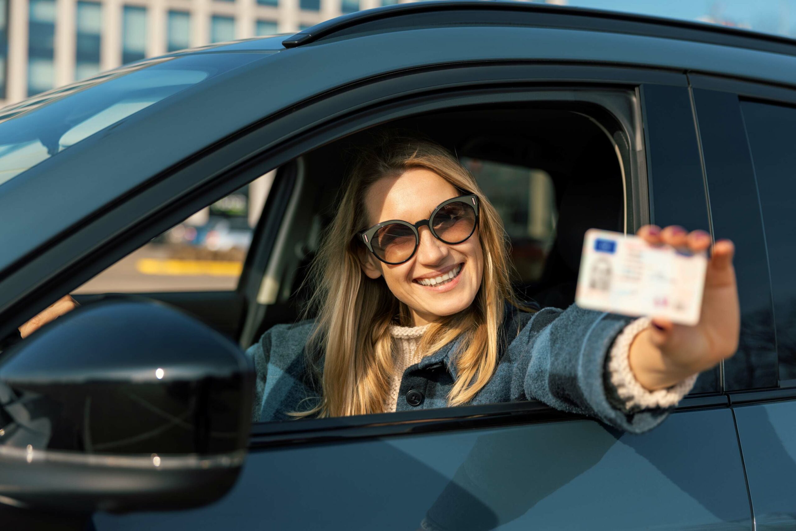 Eine Autofahrerin hält einen EU-Führerschein aus dem geöffneten Autofenster.