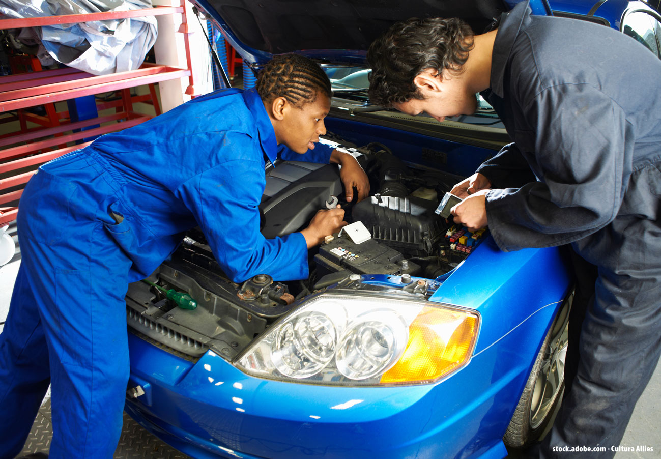 Deux personnes penchés sur le moteur d'une voiture bleue pour effectuer des réparations