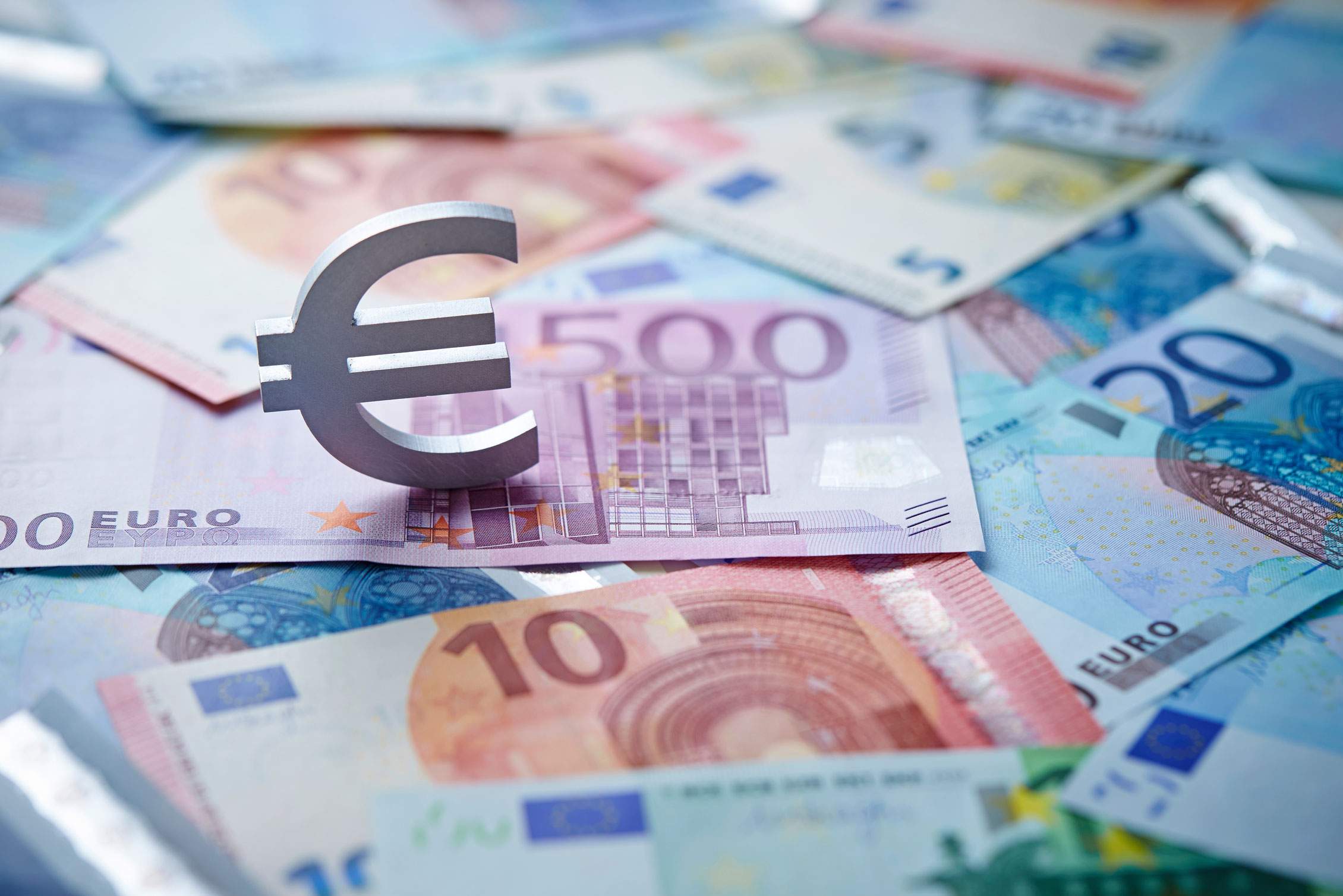 Euroscheine liegen kreuz und quer übereinander. Darauf steht ein Eurozeichen.
