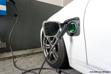 Ein weißes Elektroauto wird per Kabel an einer Wallbox geladen.