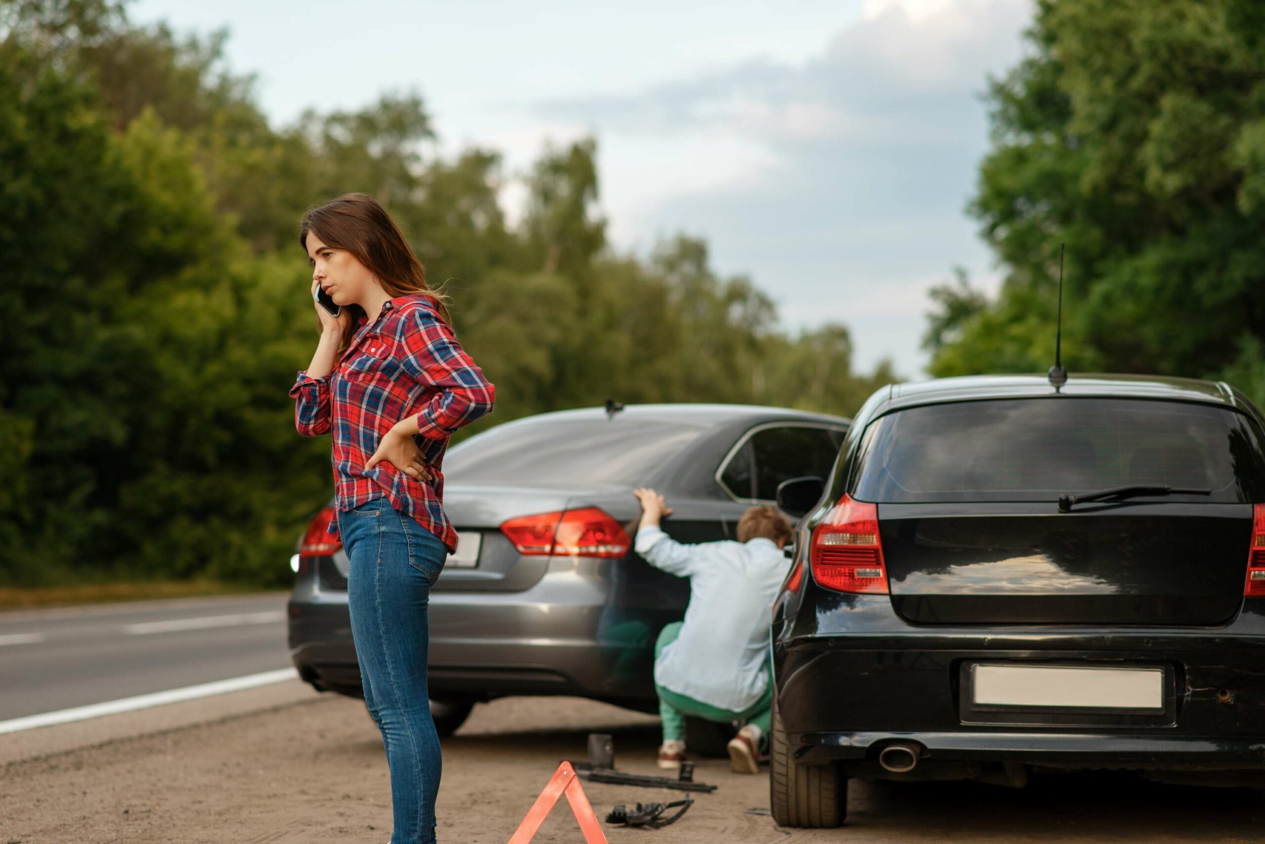 Am Straßenrand stehen zwei Autos nach einem Unfall. Eine Frau telefoniert, während ein Mann nach den Fahrzeugen schaut.
