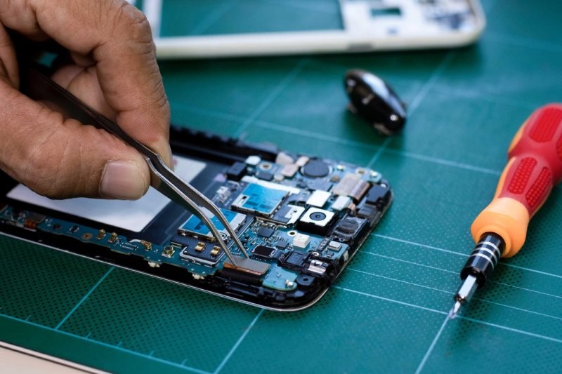 Feinarbeit am geöffneten Smartphone: Eine Person repariert Bauteile mit einer Pinzette.