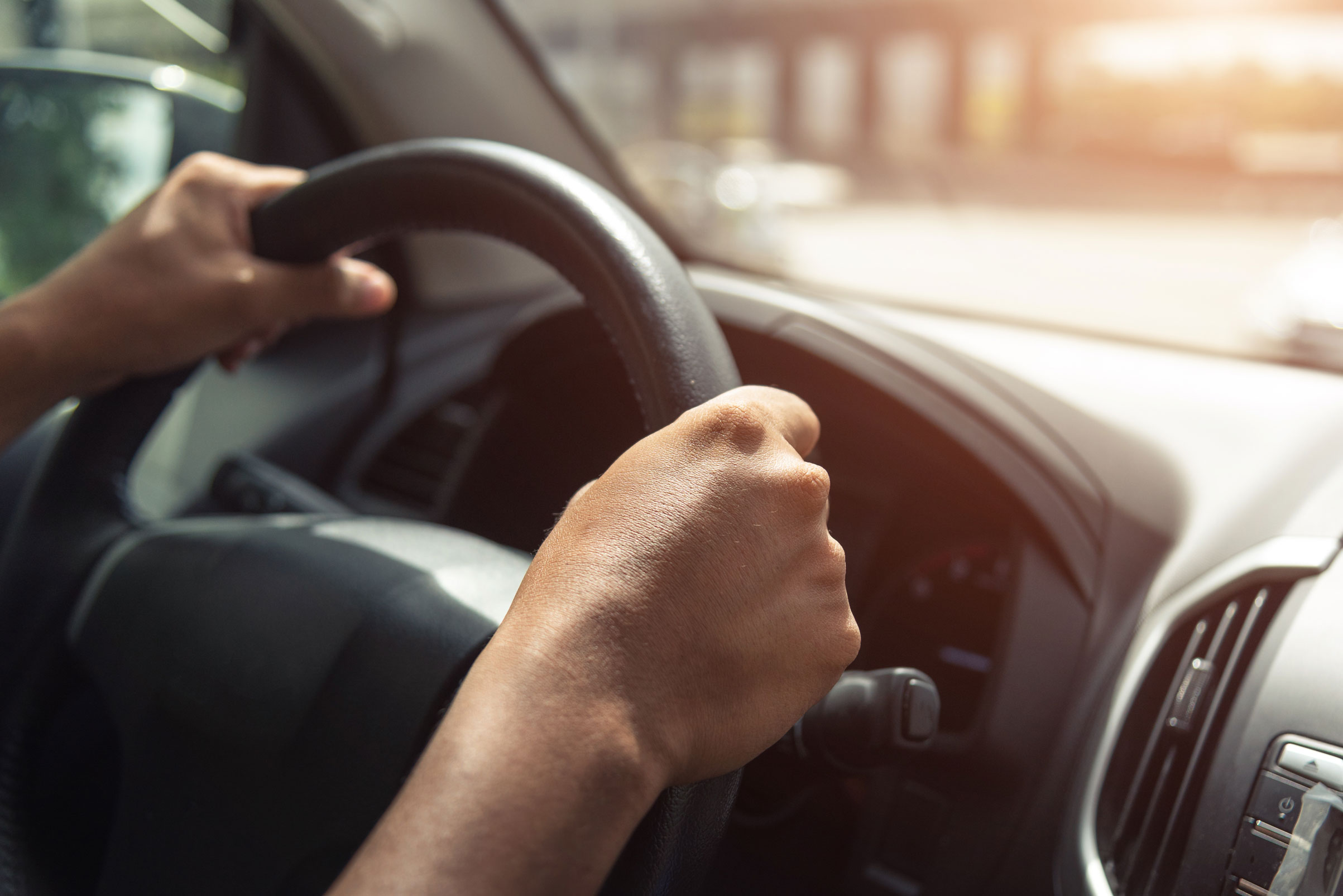 Innenansicht eines fahrenden Autos. Eine Person hält das Lenkrad mit beiden Händen.