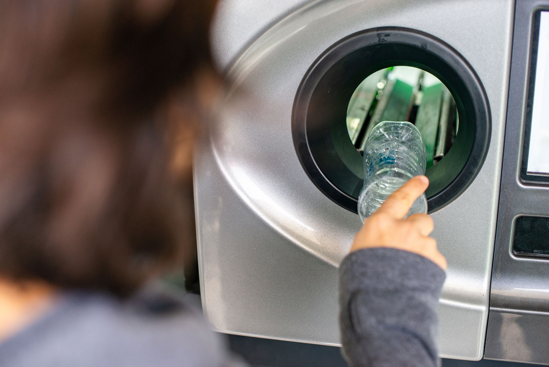 Une personne dépose une bouteille en plastique dans un automate afin de récupérer la consigne.