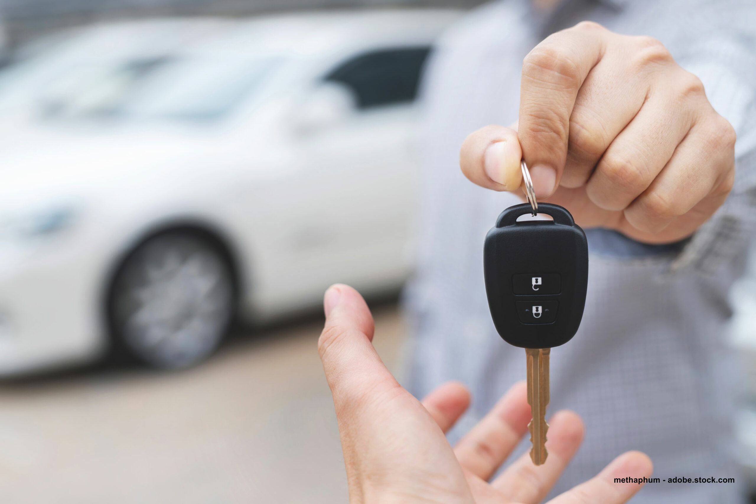 Nahaufnahme einer Hand, die einen Autoschlüssel einer anderen Hand übergibt.
