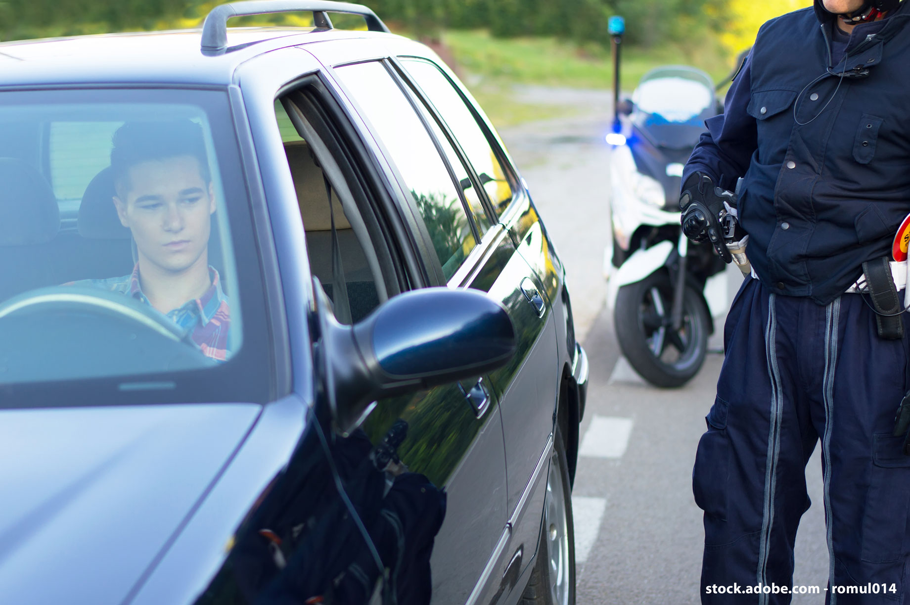 Ein junger Autofahrer wird von der Polizei kontrolliert. Im Hintergrund steht ein Polizeimotorrad.
