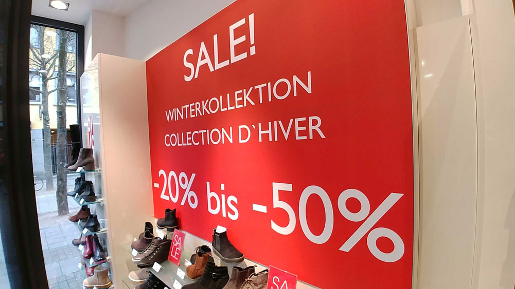 Un panneau écrit en allemand sur le mur d'une boutique mentionne des soldes sur la collection hiver "de -20% à -50%"..