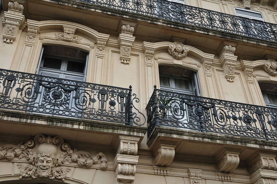 Facade d'un immeuble avec des moulures et des balcon en fer forgé.