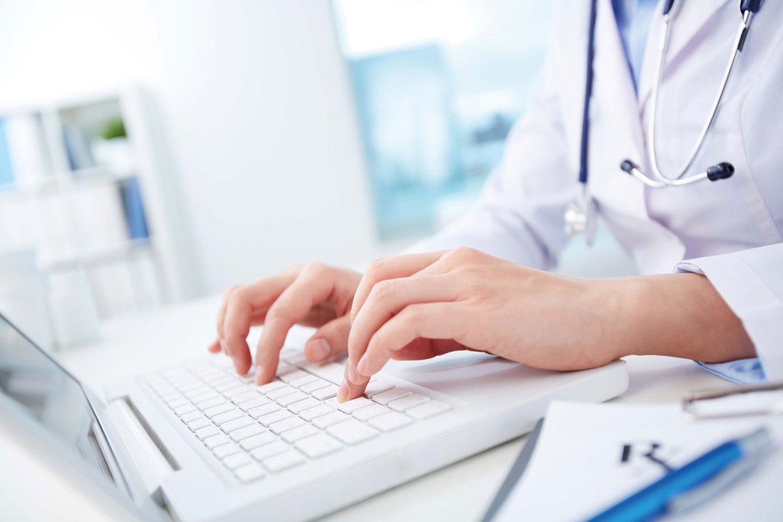 Un médecin en blouse blanche avec un stéthoscope autour du cou tape sur le clavier de son ordinateur.