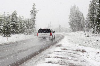 Une voiture roule sur une route au milieu d'un paysage enneigée.