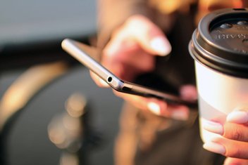 Une personne tient son smartphone dans une main, son café dans l'autre.