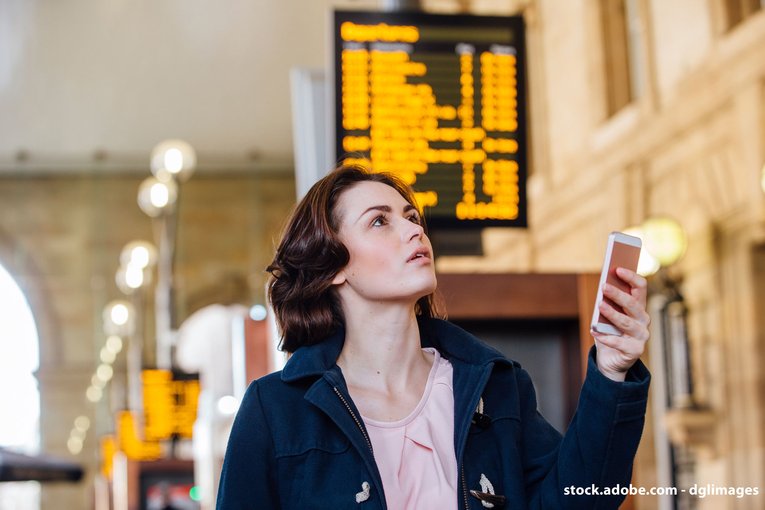 Voyageuse comparant les informations sur son smartphone et celles des panneaux d'affichage de la gare. Le Deutschlandticket est disponible uniquement en billet numérique.