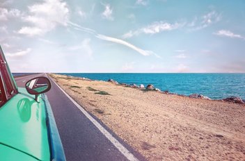 Une voiture verte roule le long d'une côte : on peut voir la mer à côté de la route.