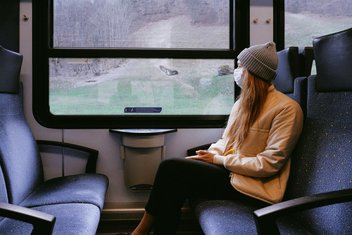 Frau sitzt mit Maske im Zug