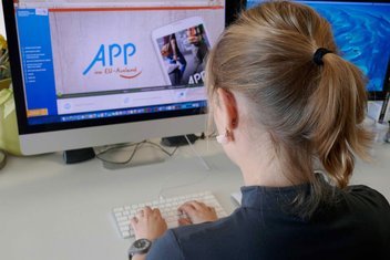 Eine junge Frau sitzt an ihrem iMac (Computer) und surft im Internet.