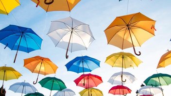 Des parapluies colorés sont suspendus ouverts sur un ciel bleu en fond.